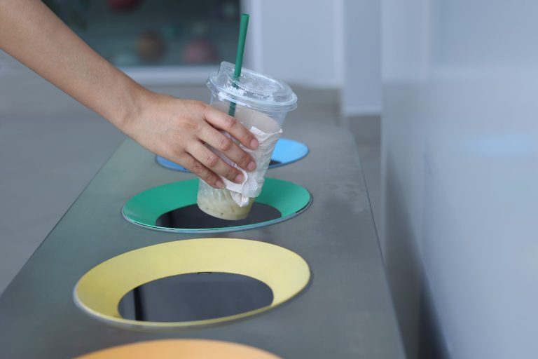 Woman hand holding throwing plastic cup in litter bin On-the-Go Recycling