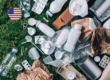 Assorted plastic, paper, and metal packaging waste on a green grass background with a U.S. flag icon, illustrating the 2026 U.S. EPR reporting requirements and SB 54 compliance for producers.