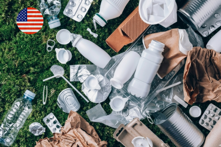 Assorted plastic, paper, and metal packaging waste on a green grass background with a U.S. flag icon, illustrating the 2026 U.S. EPR reporting requirements and SB 54 compliance for producers.