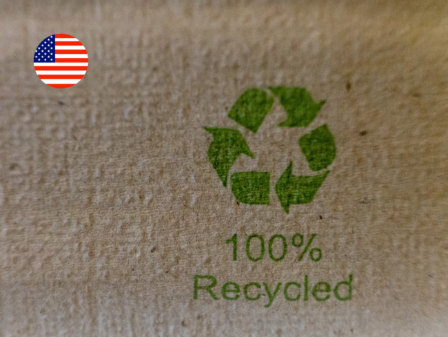 Close-up of a "100% Recycled" label printed on cardboard packaging with a US flag icon, illustrating California's packaging bills targeting recycled content and compostable labelling claims.