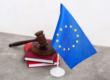 European Union flag beside a judge's gavel and law books, symbolizing the EU infringement processes towards 14 member states.