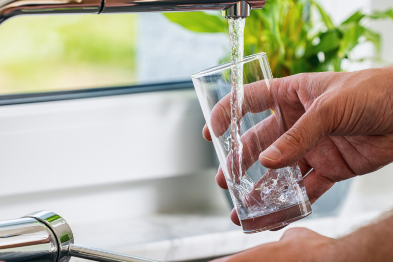 Glass being filled with drinking water from a kitchen tap, illustrating the new EU rules for products in contact with drinking water from 31 December 2026.